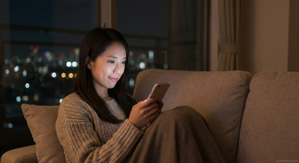 夜のリビングでスマホを見つめる若い女性